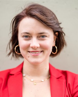 Eine Frau mit kurzen, braunen Haaren trägt ein rotes Blazer-Jackett und goldene Ohrringe. Sie lächelt freundlich in die Kamera.