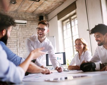 Angewandte Psychologie Berufsmöglichkeiten Eine Gruppe von fünf Personen in einem Besprechungsraum diskutiert und arbeitet an Dokumenten. Ein Mann präsentiert aktiv, während die anderen aufmerksam zuhören und Notizen machen.