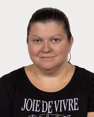Eine Frau mit kurzen, dunklen Haaren trägt ein schwarzes T-Shirt mit dem Aufdruck „JOIE DE VIVRE“ und schaut direkt in die Kamera.
