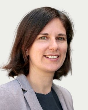 Eine Frau mit schulterlangen, braunen Haaren und einem grauen Blazer lächelt freundlich in die Kamera.