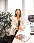 Eine Frau mit Headset sitzt an einem Schreibtisch und arbeitet am Computer, während sie in einem modernen Büro umgeben von Pflanzen ist.