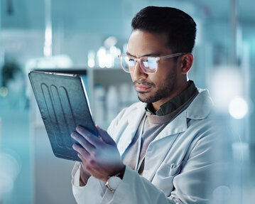 Ein Wissenschaftler in einem Laborkittel betrachtet konzentriert ein Tablet, während er in einem modernen Labor arbeitet.