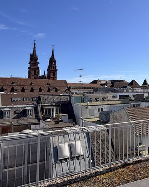 Blick auf die Dächer einer Stadt mit zwei markanten Türmen im Hintergrund und klar blauem Himmel.