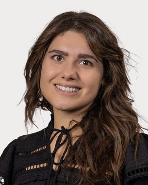 Eine lächelnde Frau mit langen, lockigen Haaren trägt ein schwarzes Oberteil mit dekorativen Details.