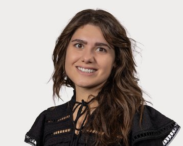 Eine lächelnde Frau mit langen, lockigen Haaren trägt ein schwarzes Oberteil mit dekorativen Details.