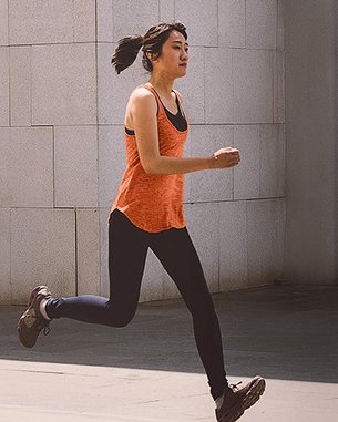Eine Frau in einem orangefarbenen Top und schwarzen Leggings läuft dynamisch in einem modernen, minimalistischen Umfeld.