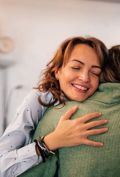 Zwei Frauen umarmen sich herzlich in einem modernen Raum, lächelnd und mit einem Gefühl von Nähe und Verbundenheit.