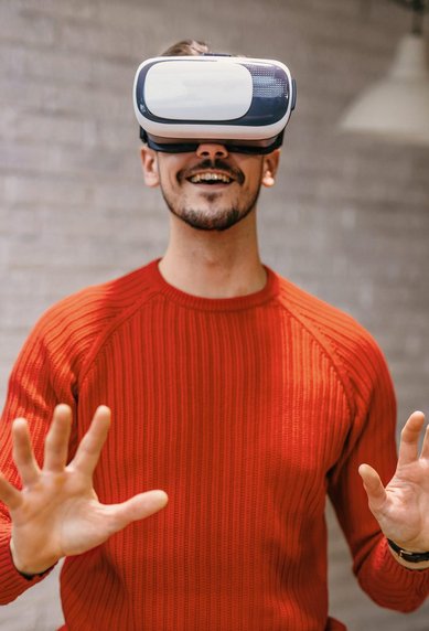Mann trägt eine Virtual-Reality-Brille und hebt die Hände, als ob er mit einer virtuellen Umgebung interagiert.