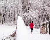 Eine Person in einem roten Oberteil joggt auf einem verschneiten Weg, der zu einer Brücke führt, umgeben von schneebedeckten Bäumen.