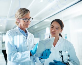 Zwei Wissenschaftlerinnen in Laborkitteln betrachten gemeinsam ein Tablet in einem modernen Labor.
