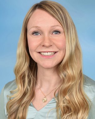 Eine lächelnde Frau mit langen, blonden Haaren trägt eine Halskette. Der Hintergrund ist hellblau.