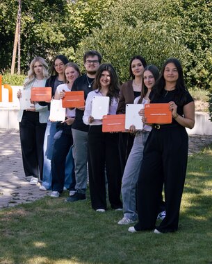 Gruppe von sieben Personen hält Zertifikate in den Händen, posiert vor einem SRH-Schild im Freien.