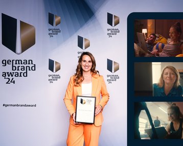 Eine Frau in einem orangefarbenen Anzug hält ein Zertifikat des German Brand Award 2024. Im Hintergrund sind mehrere Logos und Porträts von anderen Personen zu sehen.