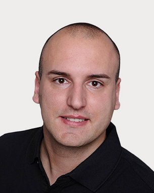 Ein Mann mit kurzem, glattem Haar trägt ein schwarzes Polohemd und schaut direkt in die Kamera. Der Hintergrund ist neutral.