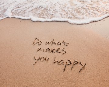Im Sand geschriebenen Text: „Do what makes you happy“, mit Wellen, die sanft den Strand berühren.