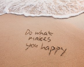 Im Sand geschriebenen Text: „Do what makes you happy“, mit Wellen, die sanft den Strand berühren.