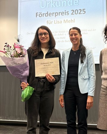 Lisa Mehl hält eine Urkunde für den Förderpreis 2025 und einen Blumenstrauß. Neben ihr steht eine weitere Person in formeller Kleidung.
