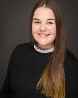 Eine junge Frau mit langen, glatten Haaren und einem freundlichen Lächeln trägt ein schwarzes Oberteil und einen weißen Kragen.