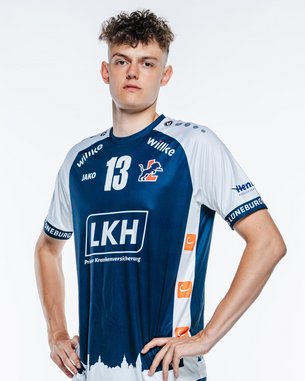 Ein junger Mann in einem blauen Handballtrikot mit der Nummer 13 steht aufrecht, mit Händen an den Hüften, in sportlicher Pose.