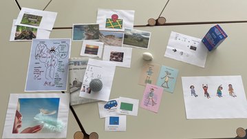 Eine Sammlung von Bildern und Zeichnungen auf einem Tisch, darunter Landschaften, Illustrationen und ein Karton mit Getränken.