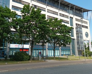 Studienzentrum Hannover | SRH Fernhochschule Modernes Bürogebäude mit großen Fenstern, umgeben von Bäumen. Im Vordergrund ist ein Schild mit der Aufschrift "JOB".