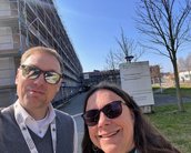 Zwei Personen posieren vor einem Gebäude mit Gerüst, das Schild der Technischen Universität ist im Hintergrund sichtbar.