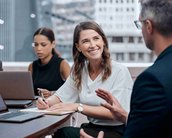 Eine Gruppe von vier Personen in einem Besprechungsraum, zwei Männer und zwei Frauen, diskutieren. Eine Frau notiert etwas und lächelt.