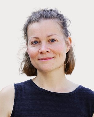 Eine Frau mit kurzen, braunen Haaren und blauen Augen trägt ein schwarzes Oberteil und lächelt freundlich in die Kamera.