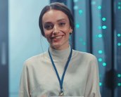 Eine lächelnde Frau hält ein Tablet in der Hand und trägt eine helle Bluse mit einem blauen Ausweisband.