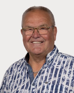 Ein älterer Mann mit Brille und einem gestreiften Hemd lächelt freundlich in die Kamera.