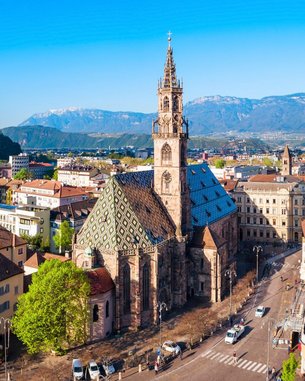 Moderne Architektur mit einem roten Rundbau und einem gläsernen Gebäude, umgeben von einer gepflegten Grünfläche und Bäumen, vor einer bergigen Kulisse.