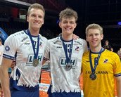 Drei Sportler stehen auf dem Spielfeld, tragen Medaillen und feiern ihren Sieg. Der Boden ist mit Konfetti bedeckt.