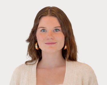 Junge Frau mit langen, braunen Haaren und großen Ohrringen, trägt einen hellen Pullover und schaut direkt in die Kamera.